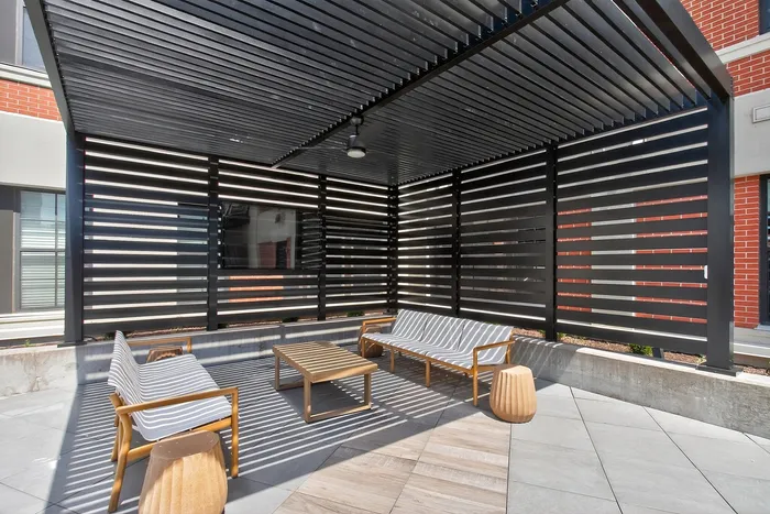 Chic outdoor patio featuring stylish wooden seating under a modern slatted pergola, offering a serene urban retreat.