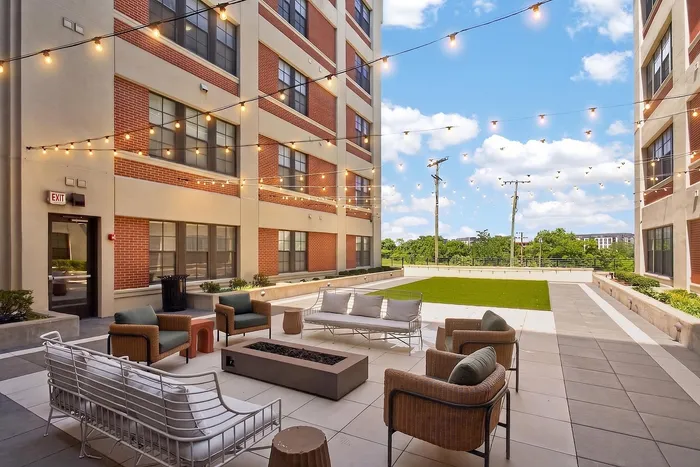 Charming apartment patio with cozy seating, string lights, and lush greenery, perfect for outdoor relaxation.