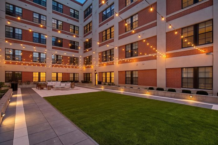 Charming courtyard with ambient string lights, modern seating, and lush green lawn at dusk.