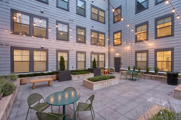 Charming apartment courtyard featuring string lights, modern seating, and lush planters for a cozy outdoor gathering space.