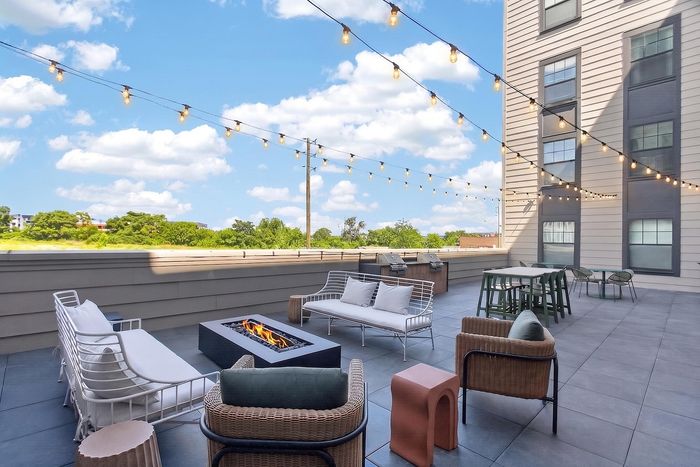 Chic rooftop terrace featuring elegant seating, cozy fire pit, and ambient string lights against a scenic backdrop.