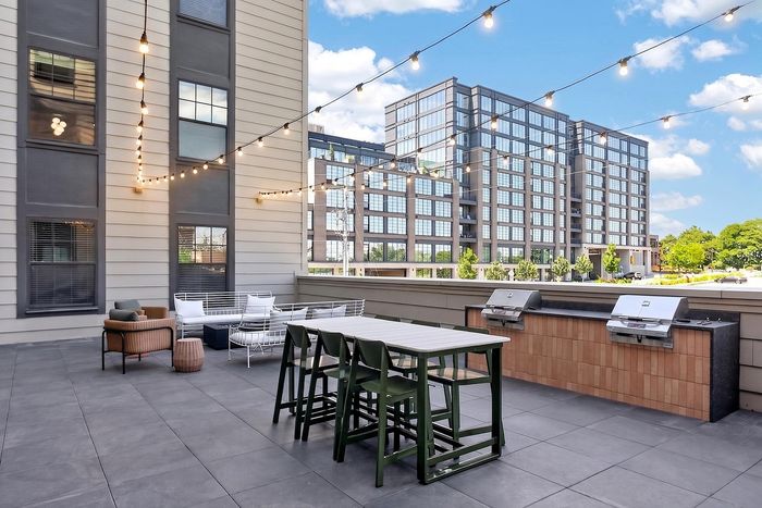 Charming urban rooftop patio with string lights, modern seating, and dual grills, offering a perfect outdoor retreat with cityscape views.