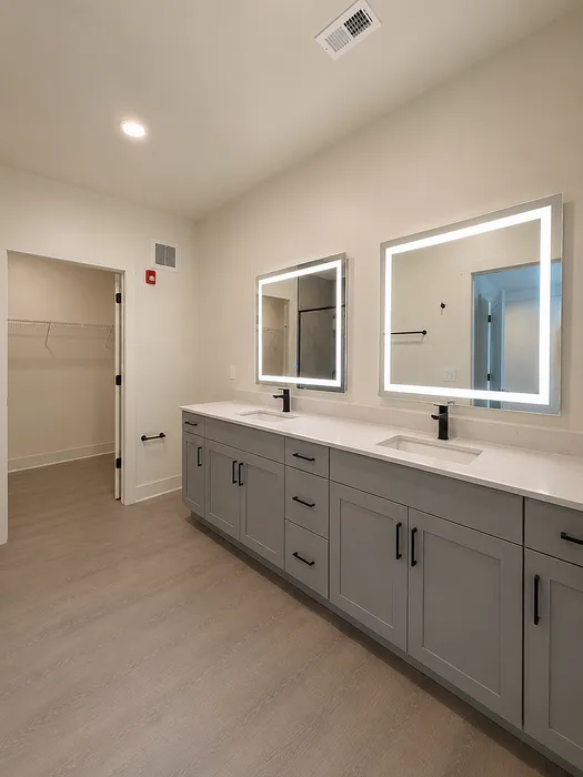 Elegant bathroom with dual sinks, illuminated mirrors, and sleek gray cabinetry.