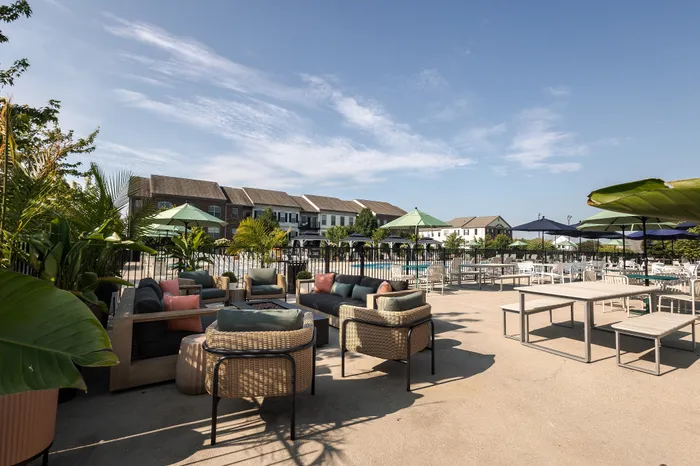 Spacious outdoor patio area with stylish seating, lush greenery, and pool view in a modern apartment community.