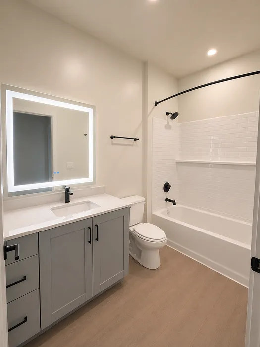 Modern bathroom featuring sleek gray vanity with integrated sink, luxurious bathtub with elegant tile wall, and illuminated mirror enhancing the bright, spacious design.