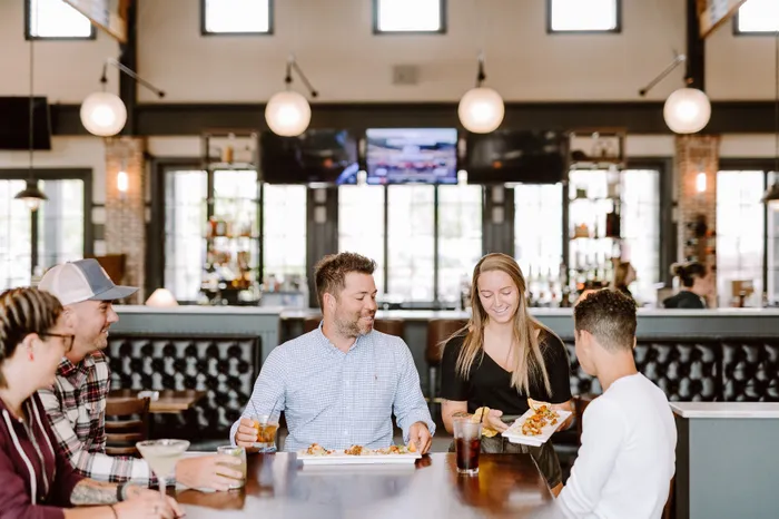 Vibrant restaurant scene with a group of friends enjoying food and drinks, highlighted by chic modern decor and warm lighting.