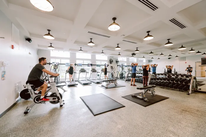 Modern fitness center with natural lighting, featuring treadmills, spinning bikes, and a variety of weightlifting equipment.