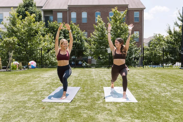 Two women practicing yoga outdoors on a sunny day in a lush green backyard, showcasing a vibrant and healthy lifestyle.