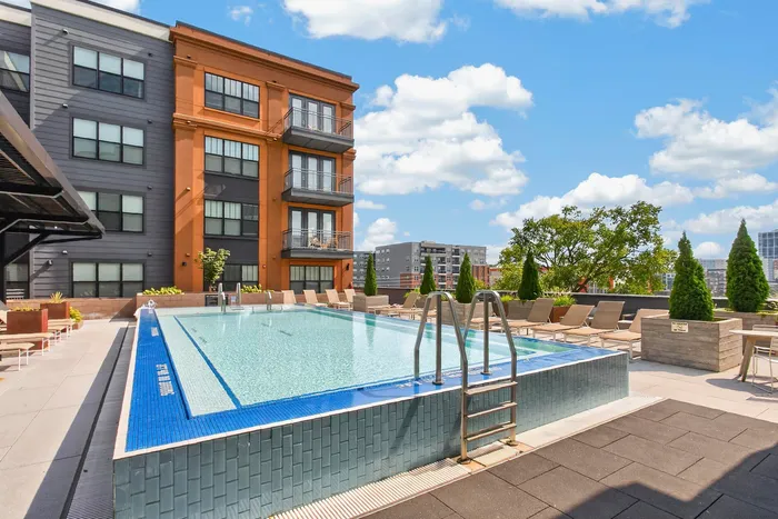 Vibrant rooftop pool area featuring modern design, surrounded by lounge chairs and lush greenery, perfect for relaxation and urban living enjoyment.