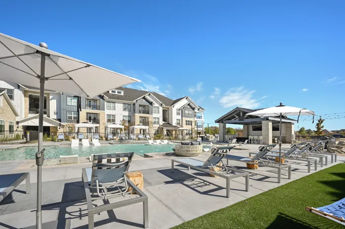 Pool area with lounge chairs, grilling area, and tables
