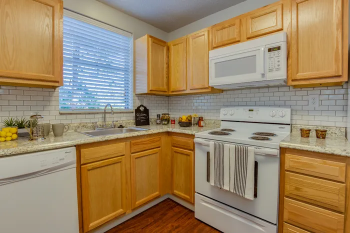 Canyon Square Apartments & Townhomes, interior, kitchen, wood cabinets, wood floor, white dishwasher, white stove/oven, white microwave, window over sink