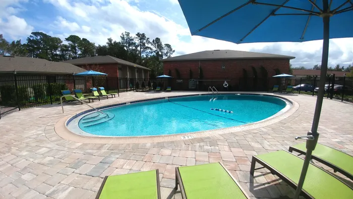 Canyon Square Apartments & Townhomes, exterior, sparkling blue pool, green lounge chairs, blue umbrella, brick buildings,