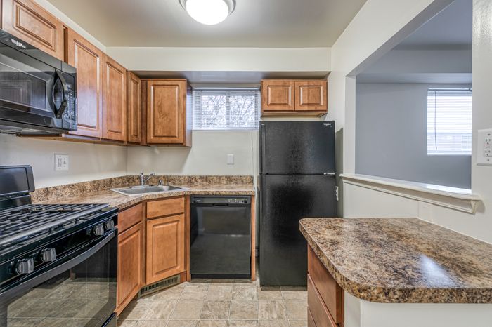 Crain Court Apts, Interior, Kitchen, Breakfast bar, honey color cabinets, window in kitchen, mrble like counter tops, Black appliances, Fridge, gas range,microwave, dishwasher, GFI outlet