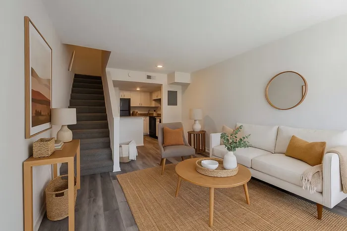 Main level of townhome. Wood flooring. White sofa. Gray chair. Natural wood side tables. Artwork.