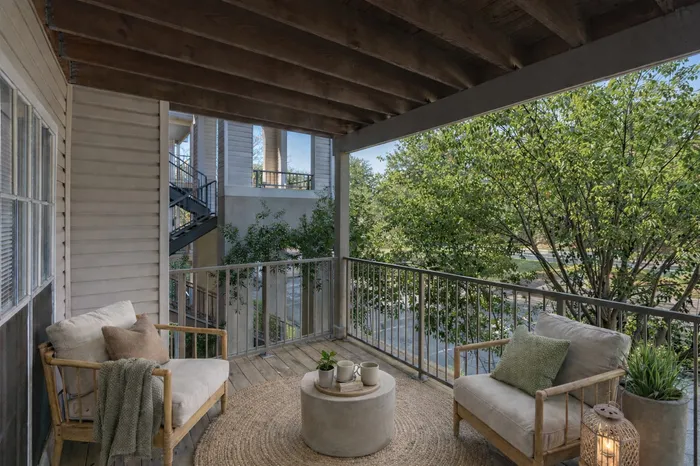 Balcony with Green Trees in View, two chairs with cushions, table, planter, and lantern