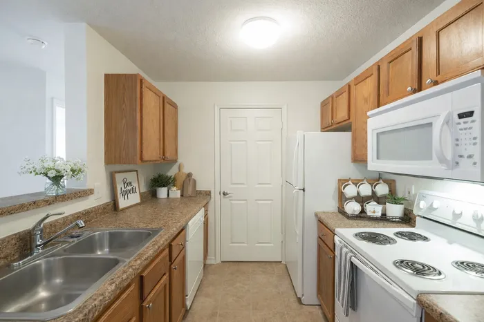Kitchen.  Oak cabinets, white appliances. White coffee mugs. Flowers in a clear vase.