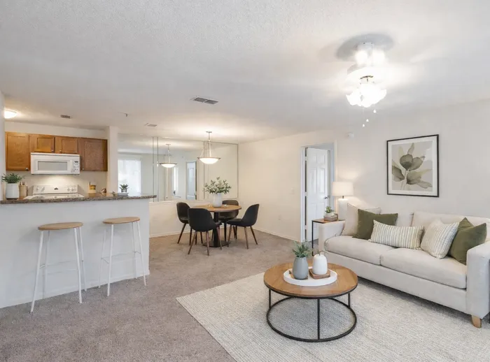 Open concept living and dining space. beige sofa with green accent pillows. wood and black coffee table. wood dining table with black chairs.