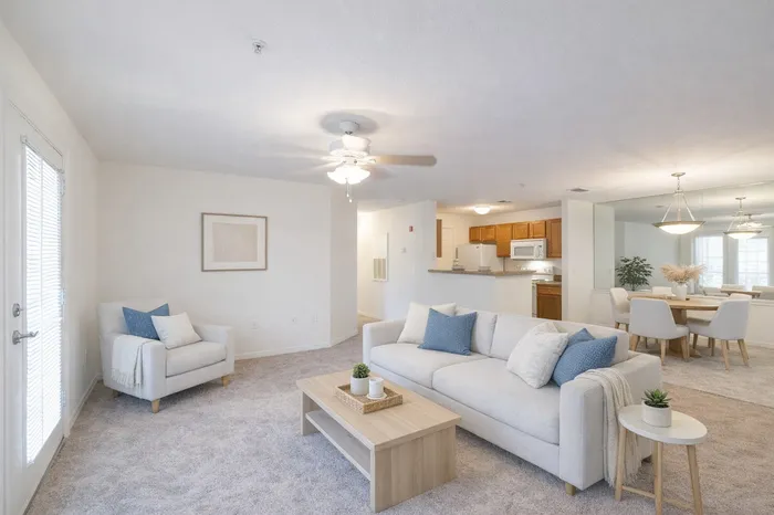 minimally styled living and dining room. Blue throw pillows. White oak coffee table. Carpet throughout.