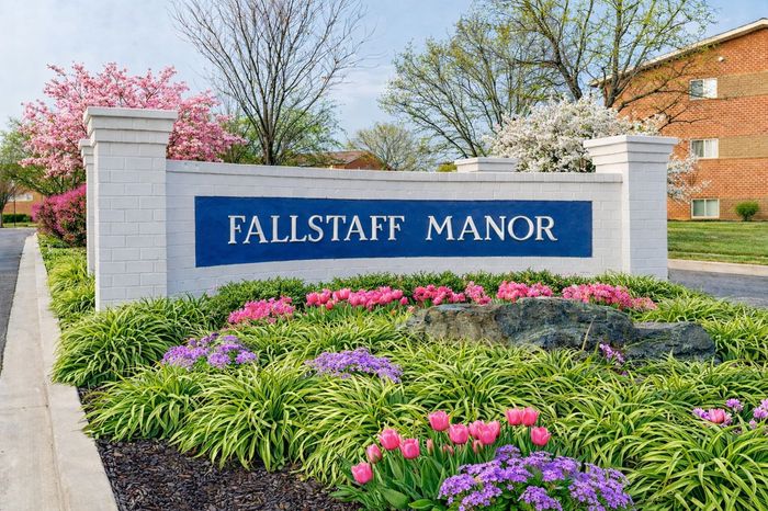 Fallstaff Entry Sign.  Blue sign surrounded by white brick.  Pink and purple flowers in front with a large rock in the middle.
