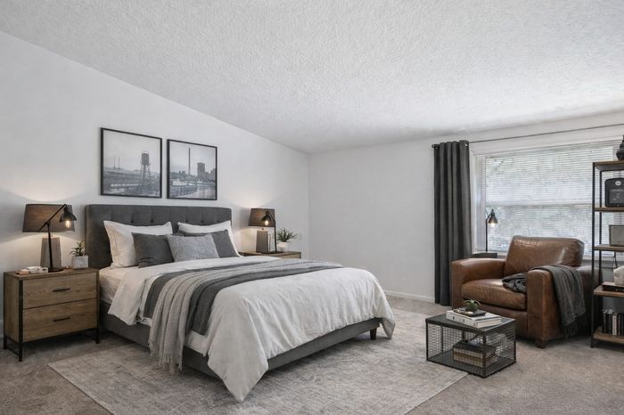 Bedroom with cathedral ceiling. brown leather arm chair. gray curtains and bedding. nightstand, shelving unit.