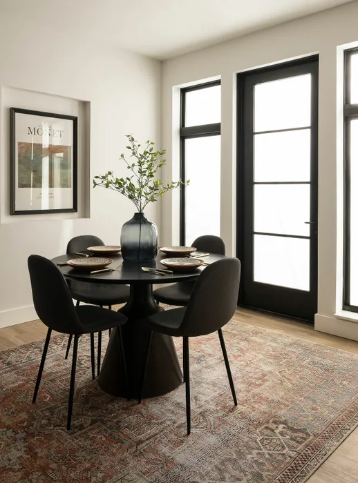 Chic dining area with a modern round table, four stylish chairs, and a decorative vase on a patterned rug.