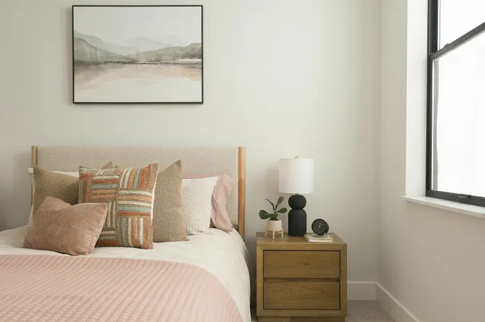 Inviting bedroom with soft-toned bedding, accent pillows, and a modern lamp on a wooden nightstand.