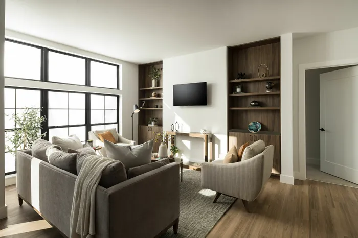 Bright and spacious living room featuring comfortable sofas, large windows, and stylish shelving units.