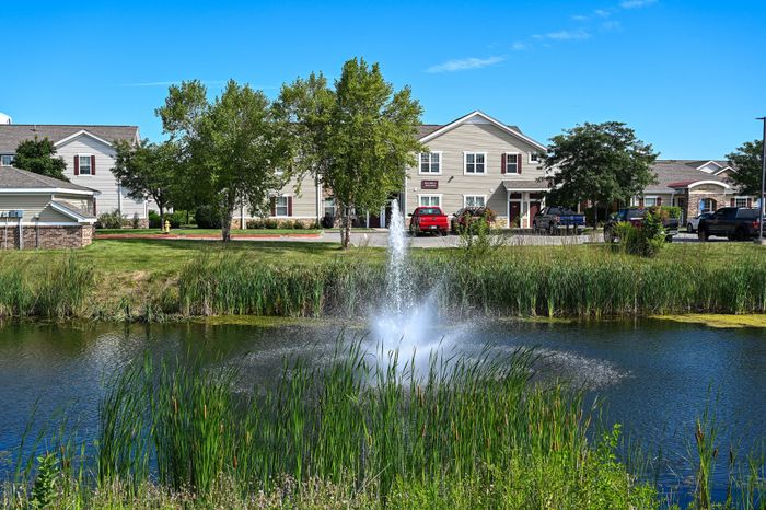 Charming residential complex surrounded by lush greenery and a serene pond with a fountain, offering a picturesque and tranquil living environment.