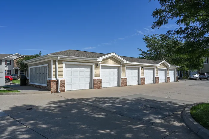 Charming residential garage units with classic white doors and brick accents under a clear blue sky.