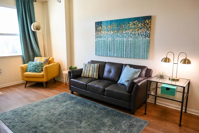 Bright and cozy living room with a modern black leather sofa, vibrant yellow armchair, and artistic wall decor, featuring stylish floor lamps and a plush area rug.