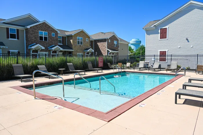 Inviting outdoor pool with sunbeds, set in a charming residential complex with brick and siding facades.