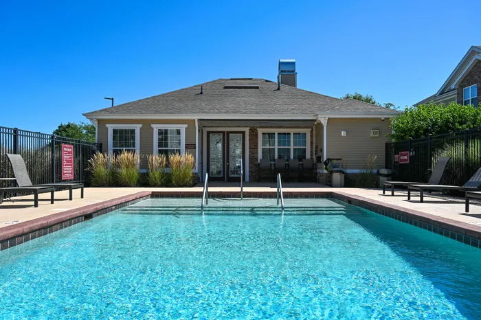 Inviting outdoor pool area with crystal-clear water, lounge chairs, and a charming clubhouse under a bright blue sky.