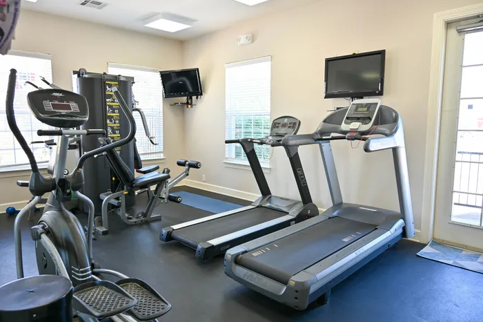 Inviting fitness center featuring treadmills, elliptical, and strength training equipment, with natural light enhancing the workout space.