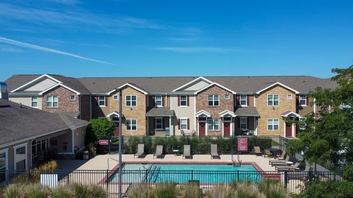 Charming townhouse complex with a sparkling pool and sun loungers, perfect for relaxation under a clear blue sky.