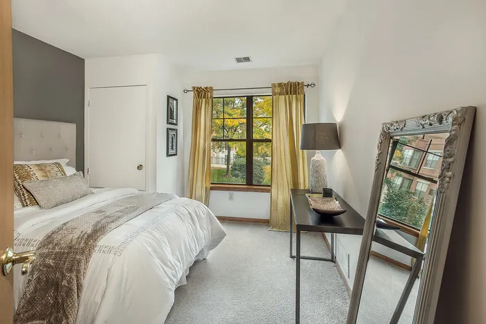 Cozy bedroom with stylish decor, featuring a plush bed, large window with lush views, elegant mirror, and chic lighting.