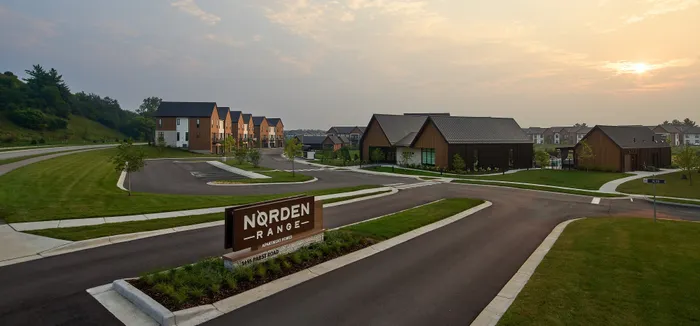 Scenic view of Norden Range apartment community with modern wooden architecture, lush greenery, and paved pathways under a serene sky.