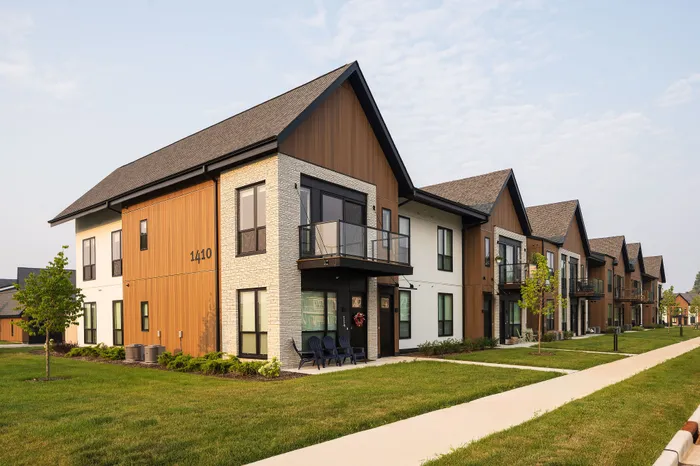 Modern apartment complex with stylish wood and stone exterior, lush green lawns, and inviting balconies.
