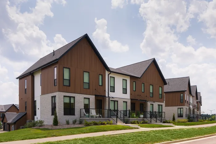 Charming modern townhouses with elegant wood and brick exteriors set against a bright sky, offering a tranquil suburban lifestyle.