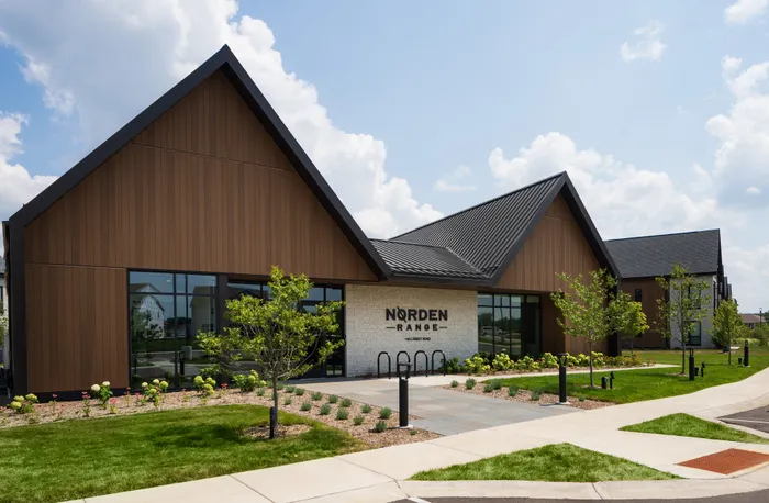 Modern architectural building with striking angular roofs, large glass windows, and beautifully landscaped greenery under a bright blue sky.