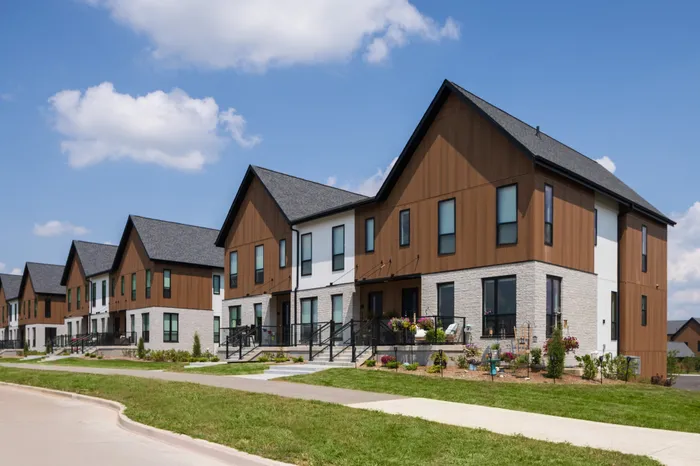 Modern townhouse complex with elegant wood and stone facades, lush greenery, and bright blue skies.