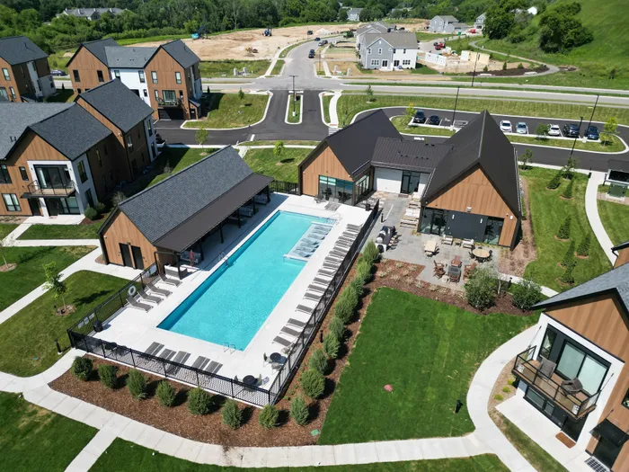 Aerial view of a contemporary apartment complex featuring a luxurious outdoor swimming pool, modern architecture, and lush landscaping.