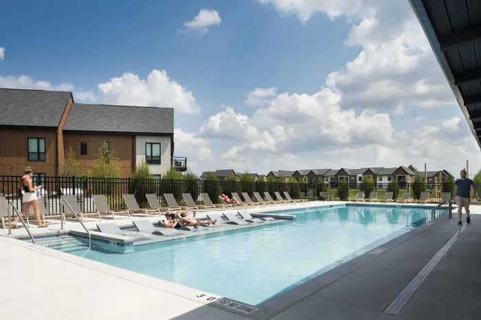 Inviting outdoor pool area featuring comfortable lounge chairs and modern apartment buildings under a sunny blue sky.