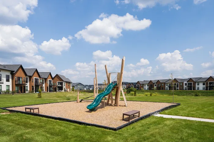 Charming residential community featuring modern townhouses with a picturesque playground under a bright blue sky.