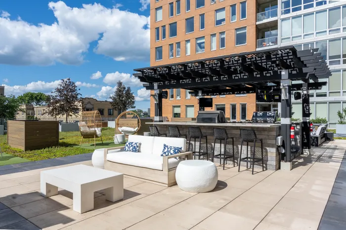 Modern outdoor patio with stylish seating, a sleek bar area under a pergola, and scenic views of a vibrant urban landscape.