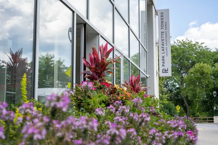 Modern apartment exterior at Park Lafayette Towers showcasing vibrant landscaped flowers and sleek glass facade.