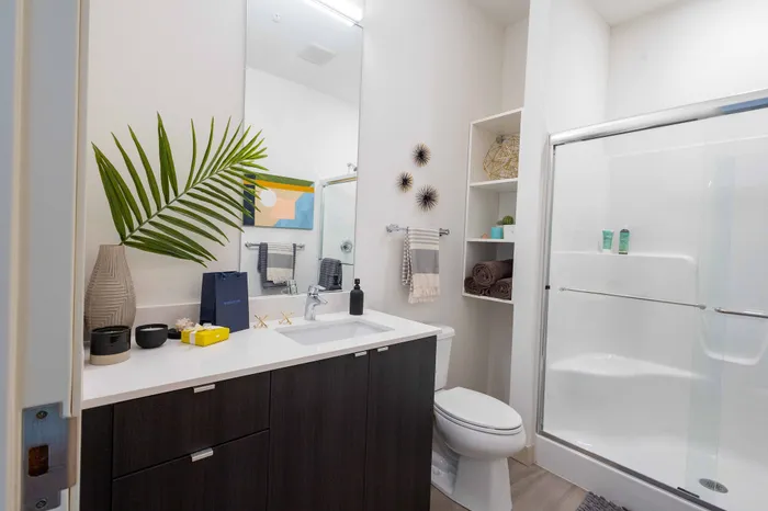 Modern bathroom with stylish vanity, elegant shower, and decorative touches including a vibrant artwork and lush plant accent.