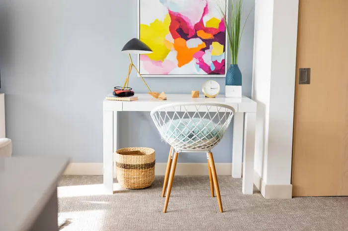 Chic home office corner with a modern white desk, stylish geometric chair, and vibrant abstract artwork, creating a bright and inspiring workspace.