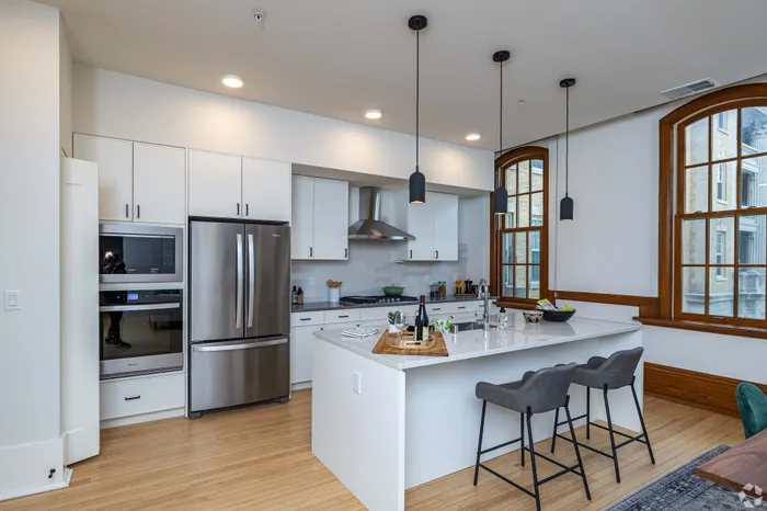 Modern kitchen with sleek stainless steel appliances, elegant pendant lighting, and a spacious island with seating by large windows.