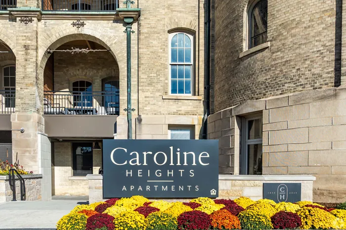 Charming Caroline Heights Apartments with rustic brick facade, elegant arches, and vibrant flower display.