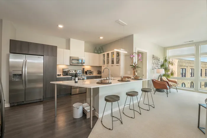Modern kitchen and living area with sleek appliances, elegant island seating, and abundant natural light.